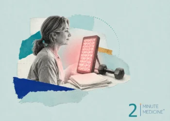 A woman using a red light therapy device while seated, surrounded by workout equipment and papers, suggesting engagement in wellness practices.